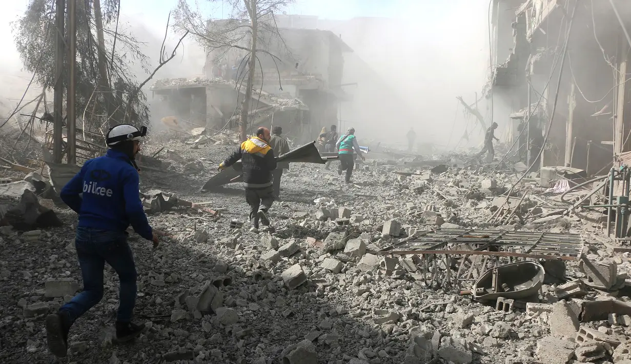 Penyelamat berlari untuk membantu korban serangan udara pasukan pemerintah di Ghouta Timur, Damaskus, Suriah, Selasa (20/2). Kelompok pemantau dan paramedis Suriah mengatakan serangan itu menewaskan 98 orang. (Syrian Civil Defense White Helmets via AP)