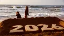 Anak-anak berjalan di belakang patung pasir karya seniman Yazed Abo Jarad yang menggambarkan angka 2026 atau tahun mendatang di Deir El-Balah, Jalur Gaza tengah pada 30 Desember 2025. Para pengungsi Palestina yang berada di Deir El-Balah, Jalur Gaza Tengah, bersiap menyambut pergantian tahun. (Bashar Taleb/AFP)