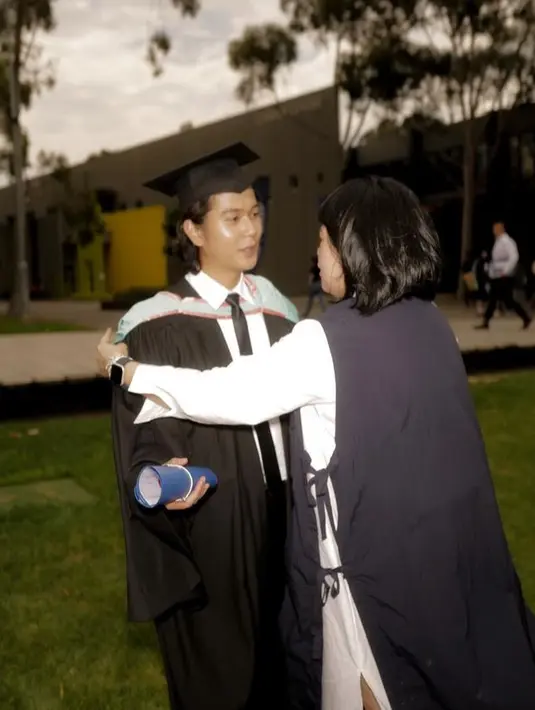 Jubah tersebut pun memilih cape warna biru dengan salur pink. Rambut gondrong pun tampak di bawah toganya. Sambil membawa tabung wisuda warna biru. [@jozz-felix]