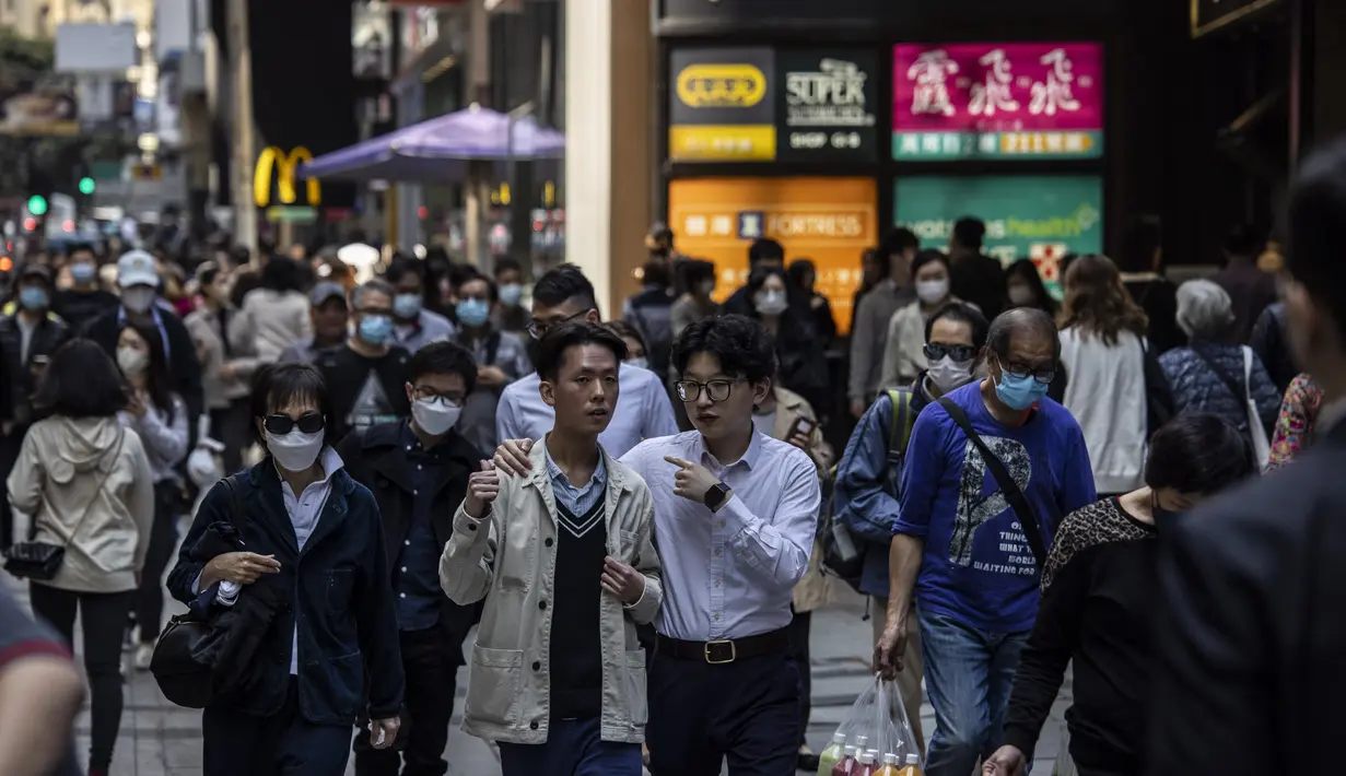 Dua pria mengobrol saat mereka berjalan melalui kawasan pusat bisnis di Hong Kong (1/3/2023). Pemerintah Hong Kong mengumumkan pelonggaran aturan Covid-19 dengan mencabut mandat penggunaan masker pada 1 Maret. Kini, warga Hong Kong bebas seperti sebelum pandemi. (AFP/Isaac Lawrence)