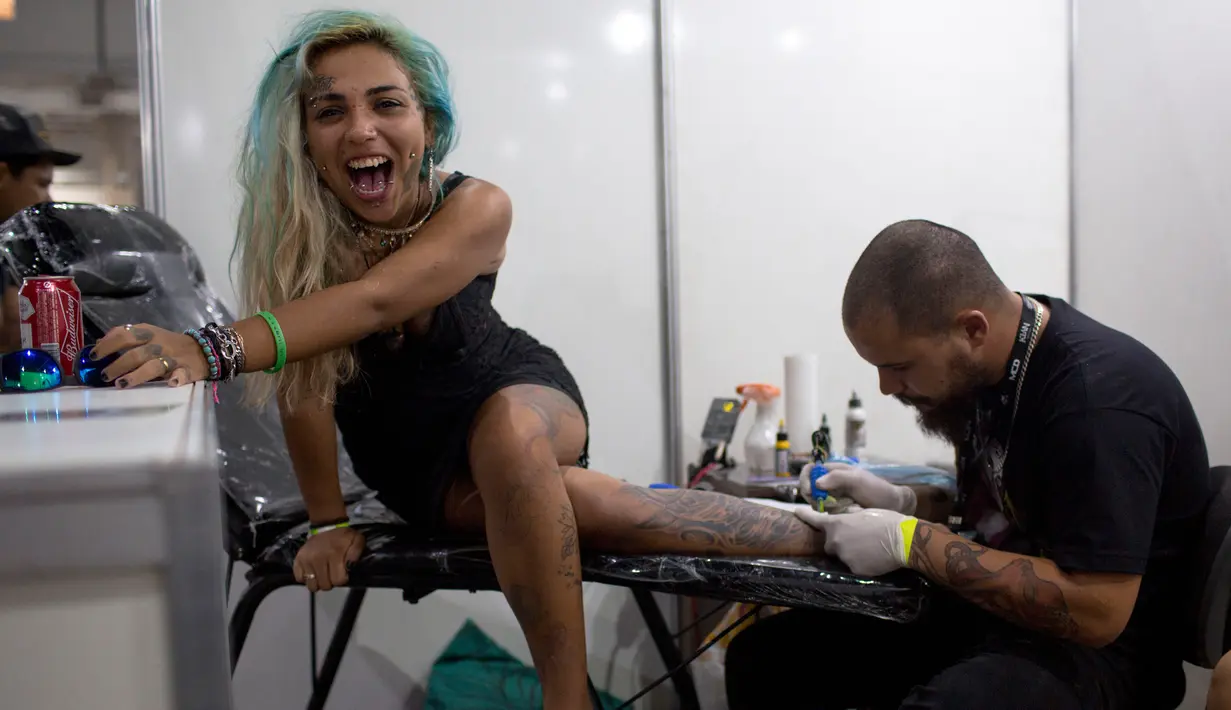 Ekspresi seorang wanita saat kakinya ditato dalam acara Tattoo Week tahunan di Rio de Janeiro, Brasil (12/1). Ajang perhelatan seniman dan penggemar tato ini diadakan setiap tahunnya di Brasil. (AFP Photo/Mauro Pimentel)