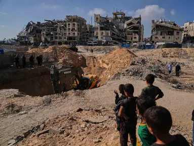 Warga Palestina menyaksikan aktivitas pekerja Mesir yang menggunakan alat berat untuk mencari jenazah para sandera di Kota Hamad, Khan Younis, di Jalur Gaza selatan, Selasa 28 Oktober 2025. (AP Photo/Abdel Kareem Hana)