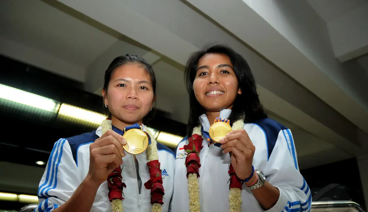 Pebulutangkis ganda putri, Greysia Polii/Nitya Krishinda, memamerkan medali emas Asian Games 2014 sesaat setelah tiba di Bandara Soekarno-Hatta, Selasa (30/9/2014). (Liputan6.com/Helmi Fithriansyah)