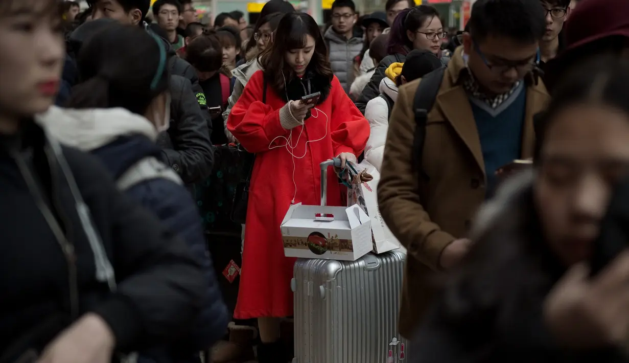 Seorang wanita bermain telepon genggam saat menungu keberangkatan kereta api di Beijing, China (23/1). Banyak dari mereka yang saat mudik membawa hadiah yang akan dibagikan pada orang tua dan kerabatnya. (AFP/Nicolas Asfouri)