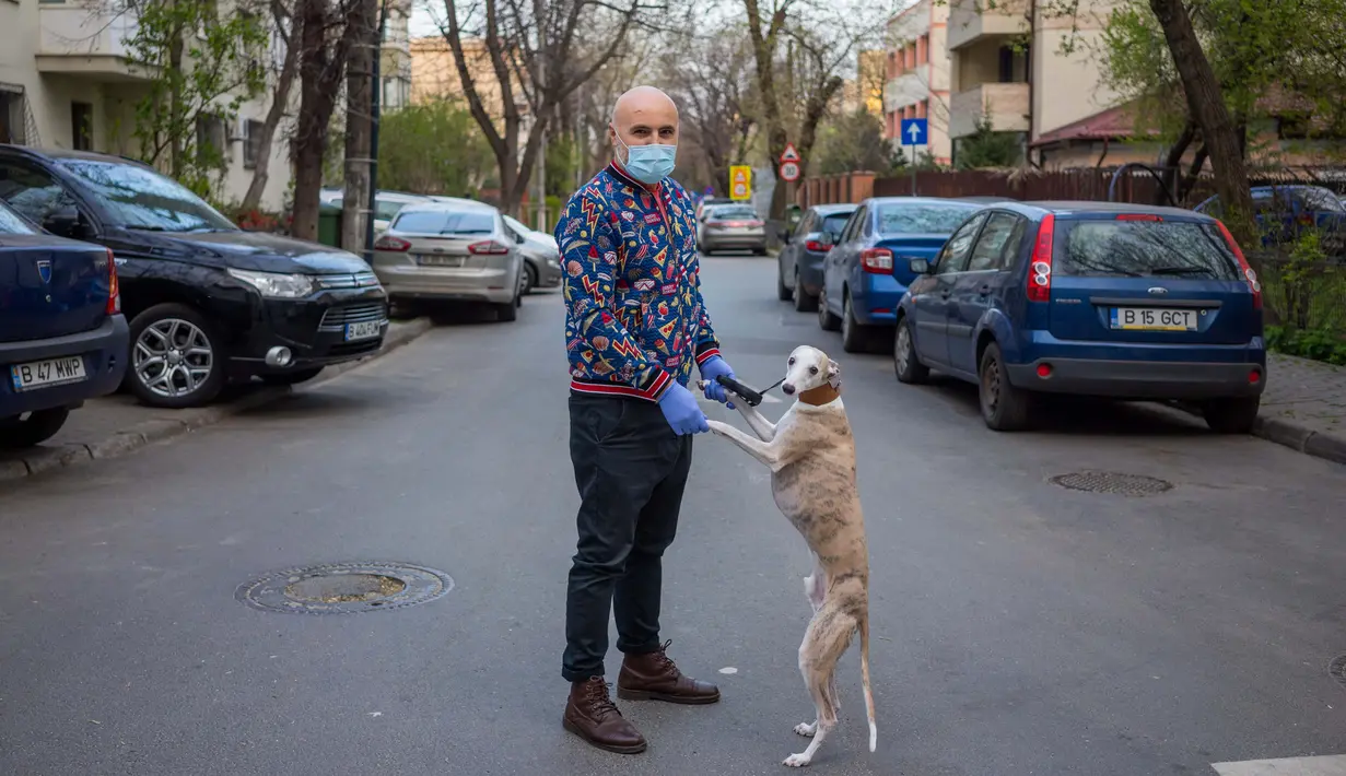 George Popa (51) berpose dengan anjing Ziggy (7) saat perjalanan di Bucharest (28/3/2020). Undang-undang militer, yang disahkan pemerintah Rumania untuk mengurangi penyebaran virus corona, menyatakan berjalan bersama anjing adalah salah satu  kegiatan yang masih diizinkan. (AFP/Andrei Pungovschi)