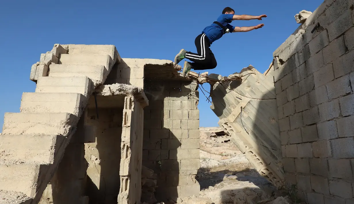 Seorang pemuda Suriah melakukan parkour di atas reruntuhan bangunan yang hancur akibat serangan pasukan rezim di kota Binnish di provinsi barat laut Idlib pada 17 Juni 2020. Parkour merupakan olahraga ketangkasan yang terdiri dari lari, melompat, salto dan berayun. (Abdulaziz KETAZ / AFP)
