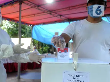 Petugas Kelompok Penyelenggara Pemungutan Suara (KPPS) dengan memakai baju hazmat membantu pemilih memasukkan kertas suara usai menggunakan hak pilihnya dalam Pilkada Tangerang Selatan 2020 di TPS 46, Paku Jaya, Serpong Utara, Rabu (9/12/2020). (merdeka.com/Arie Basuki)