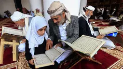 Seorang pria membaca Al-Quran bersama putrinya selama bulan Ramadan di Masjid Agung Sanaa, Yaman, Minggu (26/4/2020). Masjid Agung Sanaa bagian dari Situs Warisan Dunia UNESCO. (Mohammed HUWAIS/AFP)