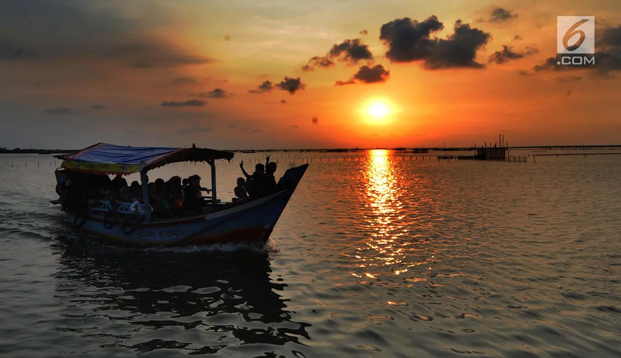 Matahari terbenam saat perahu wisatawan melewati hutan mangrove di Sungai Rindu, Desa Hurip Jaya, kecamatan Babelan, Bekasi, jumat (7/6/2019). Berkeliling naik perahu melewati kawasan hutan mangrove di Sungai Rindu ini menjadi daya tarik para wisatawan lokal. (merdeka.com/Arie Basuki)