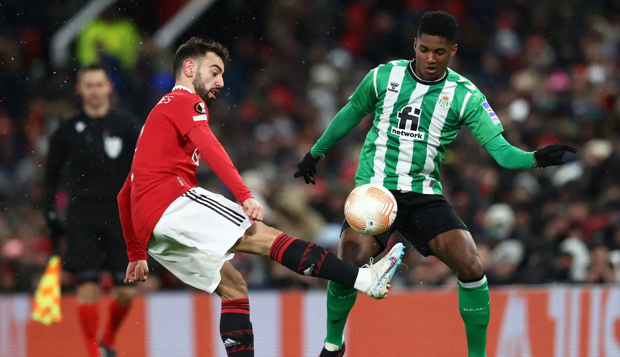 Gelandang Manchester United, Bruno Fernandes (kiri) berebut bola dengan bek Real Betis, Abner Vinicius pada laga leg pertama babak 16 besar Liga Europa 2022/2023 di Old Trafford Stadium, Manchester (9/3/2023). Bruno Fernandes telah mencetak 9 gol dan 8 assist dari 24 penampilan bersama MU dalam 3 edisi Liga Europa yang diikutinya. (AFP/Darren Staples)