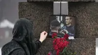 Wanita sentuh foto Alexei Navalny setelah meletakkan bunga sebagai penghormatan terakhir di  Memorial to Victims of Political Repression di St Petersburg, Rusia pada 17 Februari 2024. (AP/Dmitri Lovetsky)