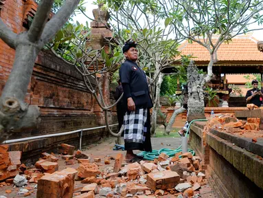 Pemuka agama memantau kerusakan pada bagian candi yang runtuh akibat gempa di Pura Lokanatha, Denpasar, Bali, Selasa (16/7/2019). Gempa Magnitudo 5,8  yang mengguncang Bali tidak menimbulkan korban jiwa, tapi sejumlah bangunan di beberapa kawasan mengalami kerusakan. (AP/Firdia Lisnawati)