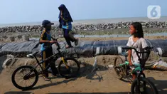 Anak-anak bermain sepeda di atas tumpukan karung pasir yang menjadi penahan datangnya gelomba dan abrasi di pesisir pantai Pisangan, Desa Cemara Jaya, Kecamatan Cibuaya, Kabupaten Karawang, Jawa Barat, Sabtu (27/5/2023). (merdeka.com/Imam Buhori)