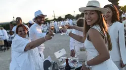 Peserta dalam balutan serba putih  bersulang sampanye saat Dinner en Blanc atau "makan malam putih" di Tuileries Gardens, Paris, Kamis (6/6/2019). Peserta acara ini harus diundang oleh mereka yang sudah terdaftar di situsnya atau mengenal salah satu penyelenggara Diner en Blanc (Lucas BARIOULET/AFP)
