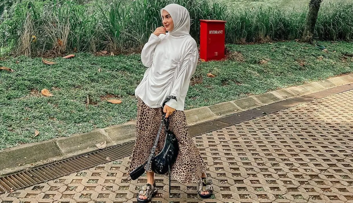 Penampilan santai Irish Bella menggunakan blouse oversize putih yang dipadukan hijab senada ini pun tak lepas dari perhatian netizen. Istri Ammar Zoni ini juga memilih menggunakan rok motif sebagai detail penampilannya. (Liputan6.com/IG/@_irishbella_)