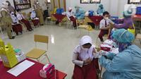 Tenaga kesehatan menyuntikkan vaksin COVID-19 kepada siswa di SDN 01 Depok, Depok, Jawa Barat, Selasa (14/12/2021). Kementerian Kesehatan mulai melaksanakan vaksinasi COVID-19 untuk anak usia 6-11 tahun dengan penggunaan vaksin Sinovac. (Liputan6.com/Herman Zakharia)