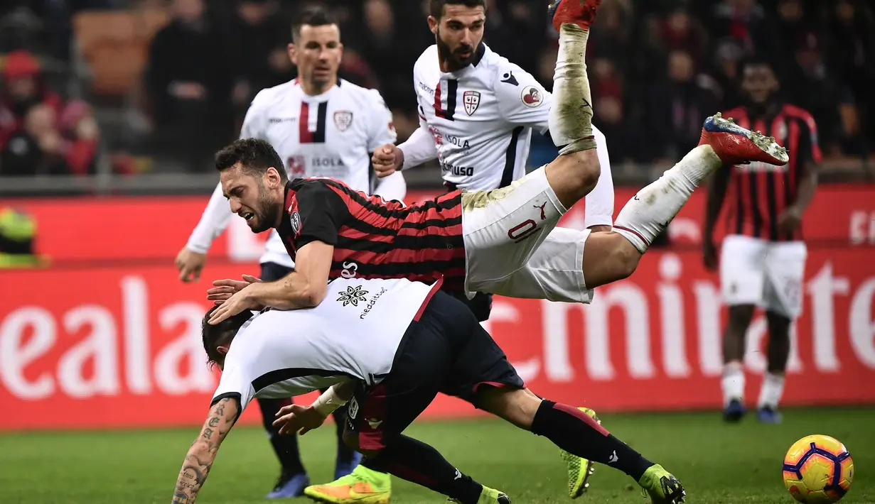 Gelandang AC Milan, Hakan Calhanoglu dijegal oleh pemain Cagliari pada laga lanjutan Serie A yang berlangsung di stadion San Siro, Milan, Senin (11/2). AC Milan menang 3-0 atas Cagliari. (AFP/Marco Bertorello)