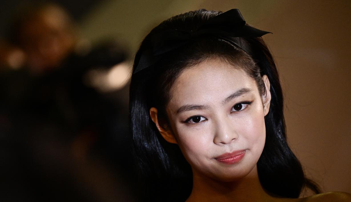 Jennie membiarkan rambutnya tergerai, mengenakan pita hitam yang serasi dengan sepatu haknya dan cocok dengan tren pita yang sedang populer saat ini. (Photo by LOIC VENANCE / AFP)