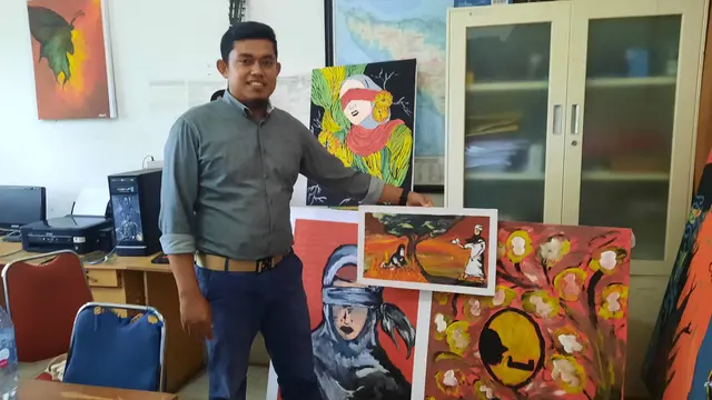 Direktur LBH Banda Aceh, Syahrul S.H., M.H., berpose di antara beberapa contoh lukisan yang akan dipajang dalam pameran dan pertunjukan seni 16HAKtP Aceh (Liputan6.com/Rino Abonita)