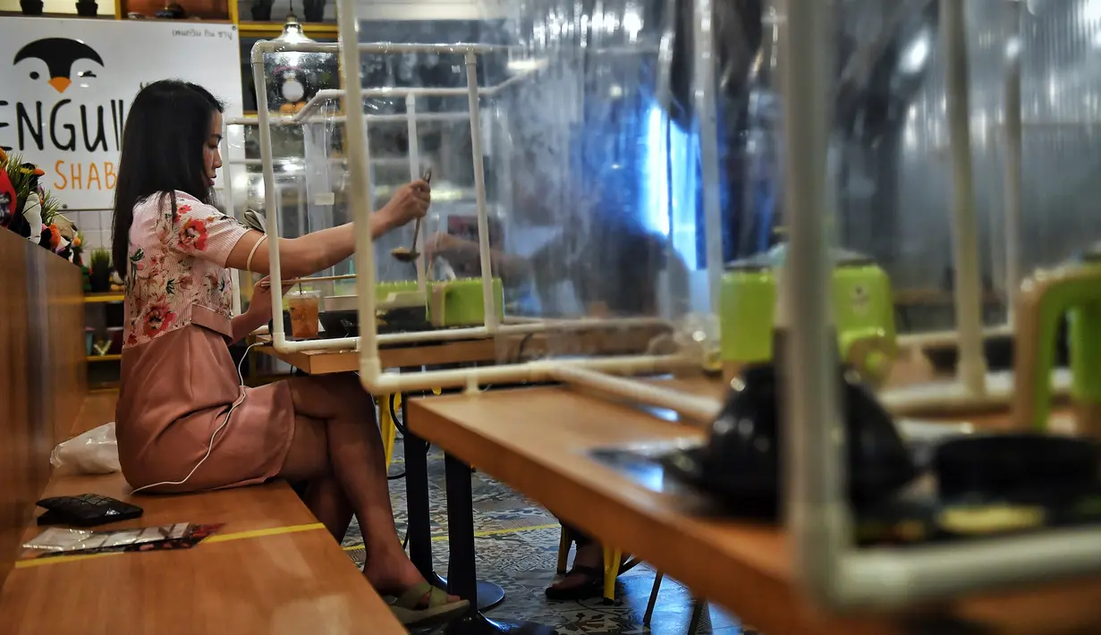 Sepasang pengunjung makan di sela-sela pembatas plastik untuk mencegah penyebaran virus corona di restoran Penguin Eat Shabu di Bangkok, 5 Mei 2020. Restoran kembali dibuka setelah Thailand memperlonggar lockdown dengan mengizinkan tempat makan menerapkan social distancing. (Lillian SUWANRUMPHA/AFP)