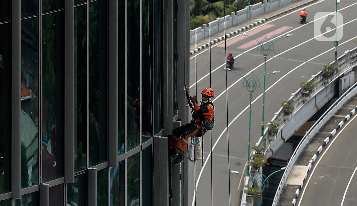 Pekerja bergelantungan membersihkan bagian luar gedung di kawasan Kuningan, Jakarta, Minggu (19/12/2021). Pekerja ini harus bergelantungan dengan seutas tali untuk membersihkan dinding-dinding gedung bertingkat yang tingginya kurang lebih mencapai 150 meter. (Liputan6.com/Johan Tallo)