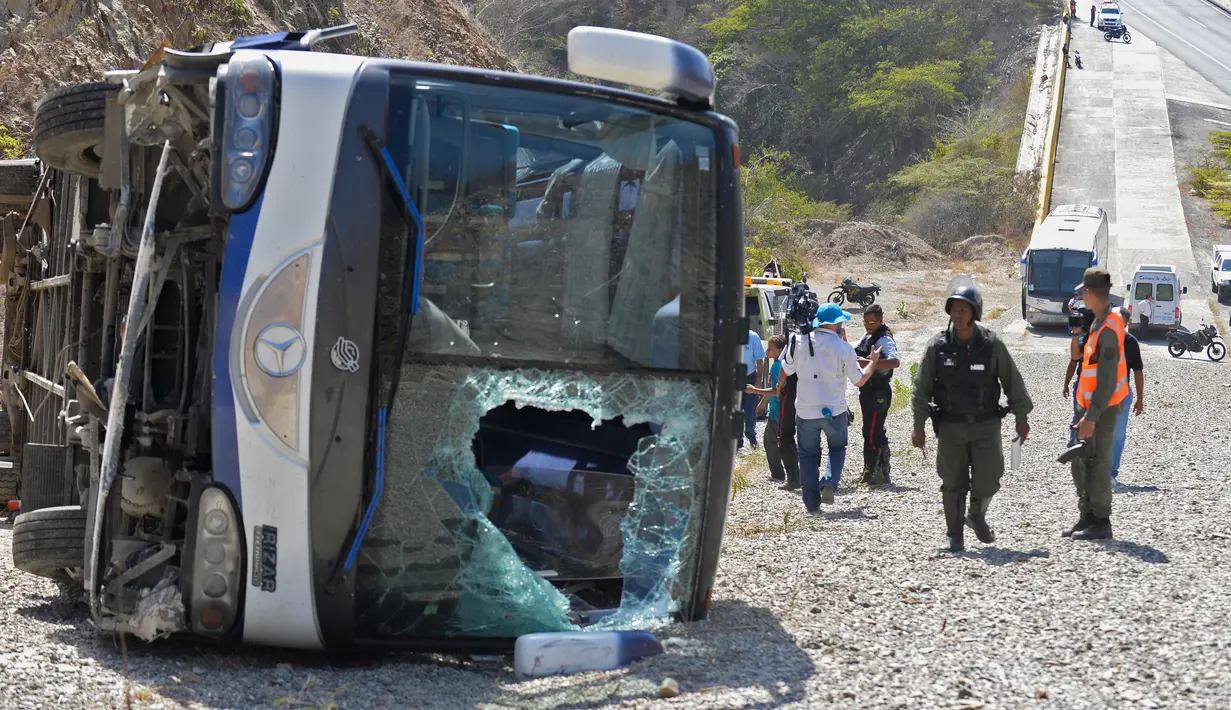 Petugas berdiri di dekat bus yang terbalik di jalan raya Caracas-La Guaira di Caracas, Venezuela, Rabu (10/2). Bus yang mengangkut pemain tim sepak bola Argentina Huracan itu kecelakaan saat menuju Bandara Internasional Simon Bolivar. (AFP/FEDERICO PARRA)