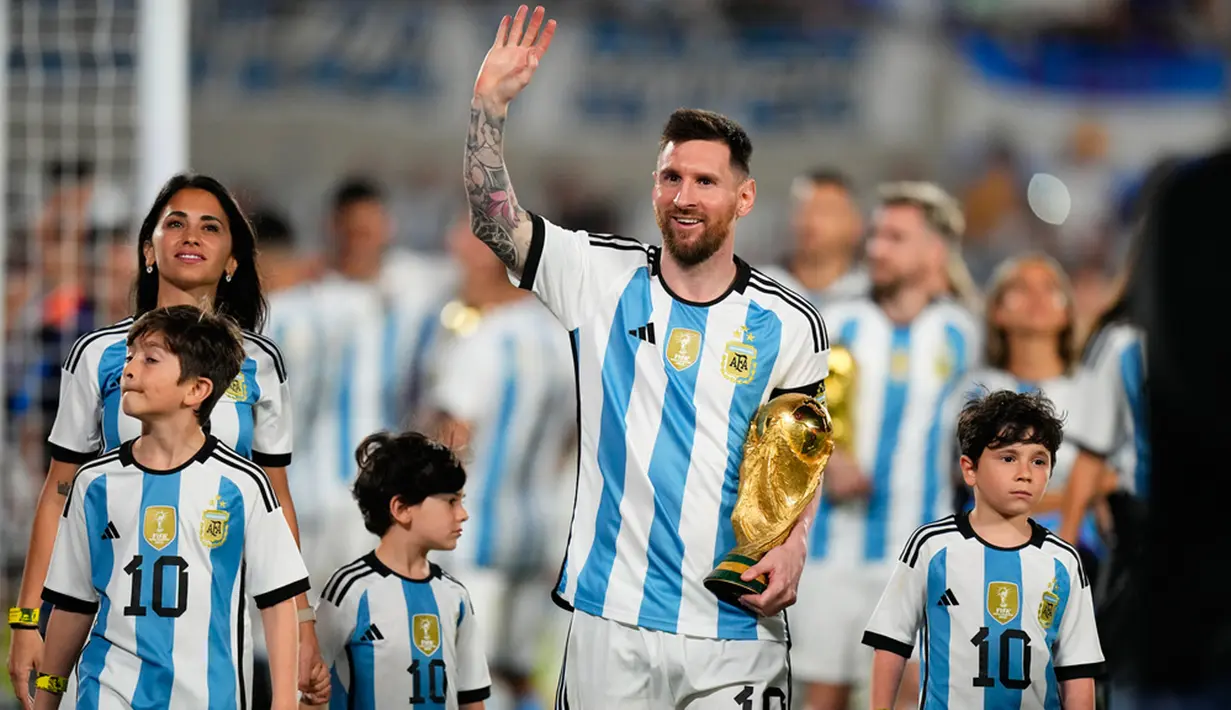 <p>Lionel Messi berjalan ditemani Antonela Roccuzzo dan anak-anak mereka dengan membawa trofi Piala Dunia sambil menyapa para penonton. (AP Photo/Natacha Pisarenko)</p>