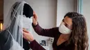 Desainer Friederike Jorzig merapikan masker buatannya di Berlin, Jerman (31/3/2020). Frederike Jorzig membuat gaun pernikahan yang dirancang lengkap dengan masker untuk menghindari penularan Covid-19 di tokonya di distrik Schoeneberg Berlin. (AFP/Odd Andersen)