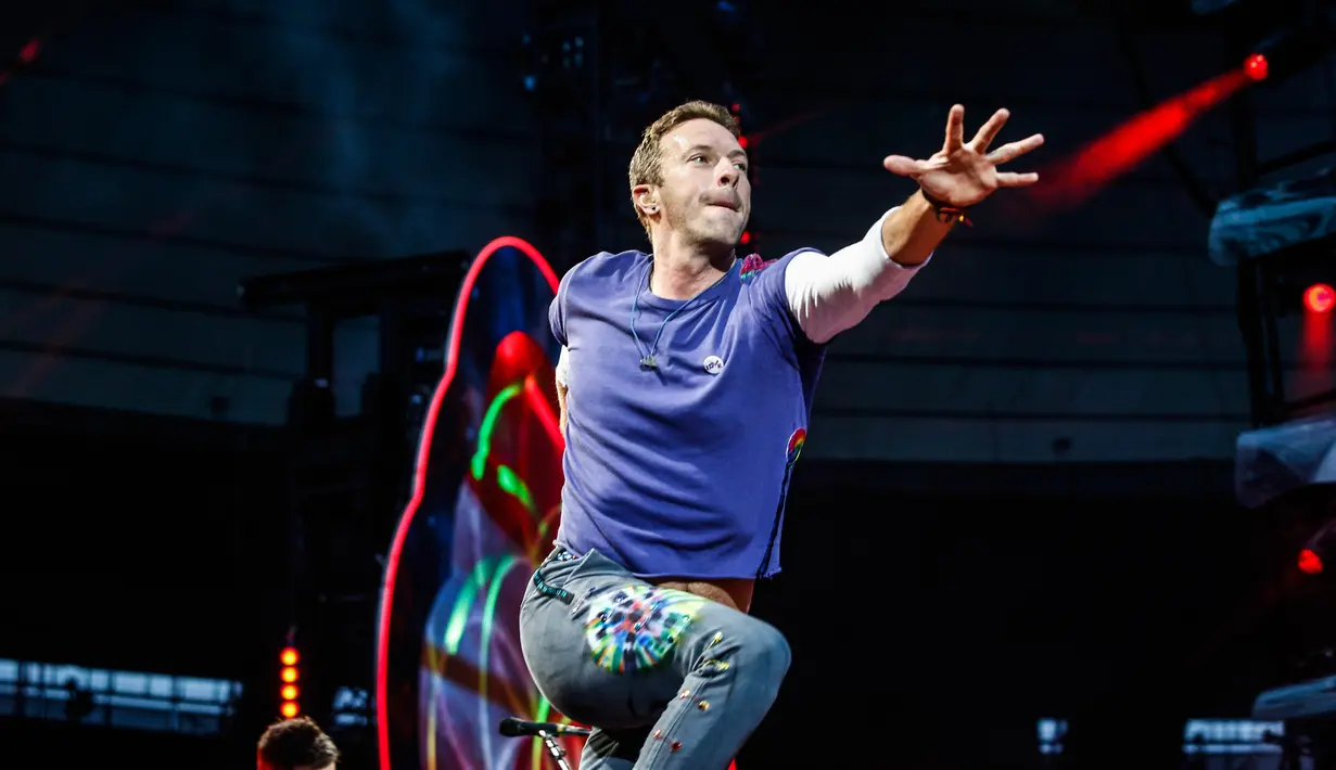 Aksi vokalis band Inggris Coldplay, Chris Martin saat tampil di The Stade de France Arena di Saint Denis, Paris, Prancis (15/7). (AFP Photo/Geoffroy Van Der Hasselt)