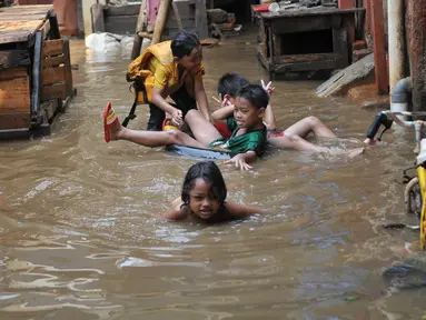 Anak-anak bermain di lokasi banjir yang merendam kawasan Kampung Pulo, Jakarta, Selasa (17/11). Kawasan di sepanjang aliran Kali Ciliwung terendam banjir sejak kemarin akibat Bendungan Katulampa yang sudah mencapai siaga satu (Liputan6.com/Gempur M Surya)