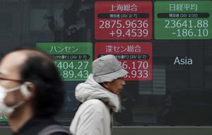 Orang-orang berjalan melewati layar monitor yang menunjukkan indeks bursa saham Nikkei 225 Jepang dan lainnya di sebuah perusahaan sekuritas di Tokyo, Senin (10/2/2020). Pasar saham Asia turun pada Senin setelah China melaporkan kenaikan dalam kasus wabah virus corona. (AP Photo/Eugene Hoshiko)