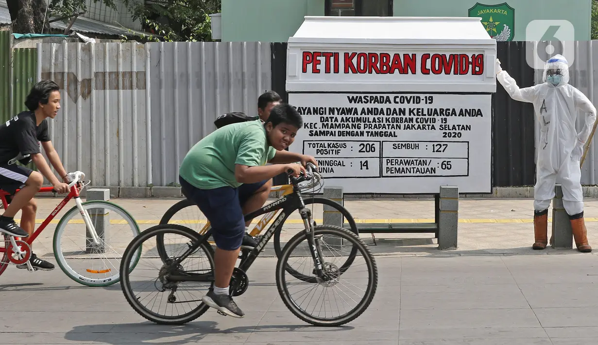 Pesepeda melintas di depan seni instalasi yang menggambarkan tenaga medis memegang peti jenazah korban COVID-19 di Kemang 1, Jakarta Selatan, Minggu (16/8/2020). Seni instalasi itu dipajang guna memberi peringatan kepada warga untuk tetap waspada terhadap COVID-19. (Liputan6.com/Herman Zakharia)