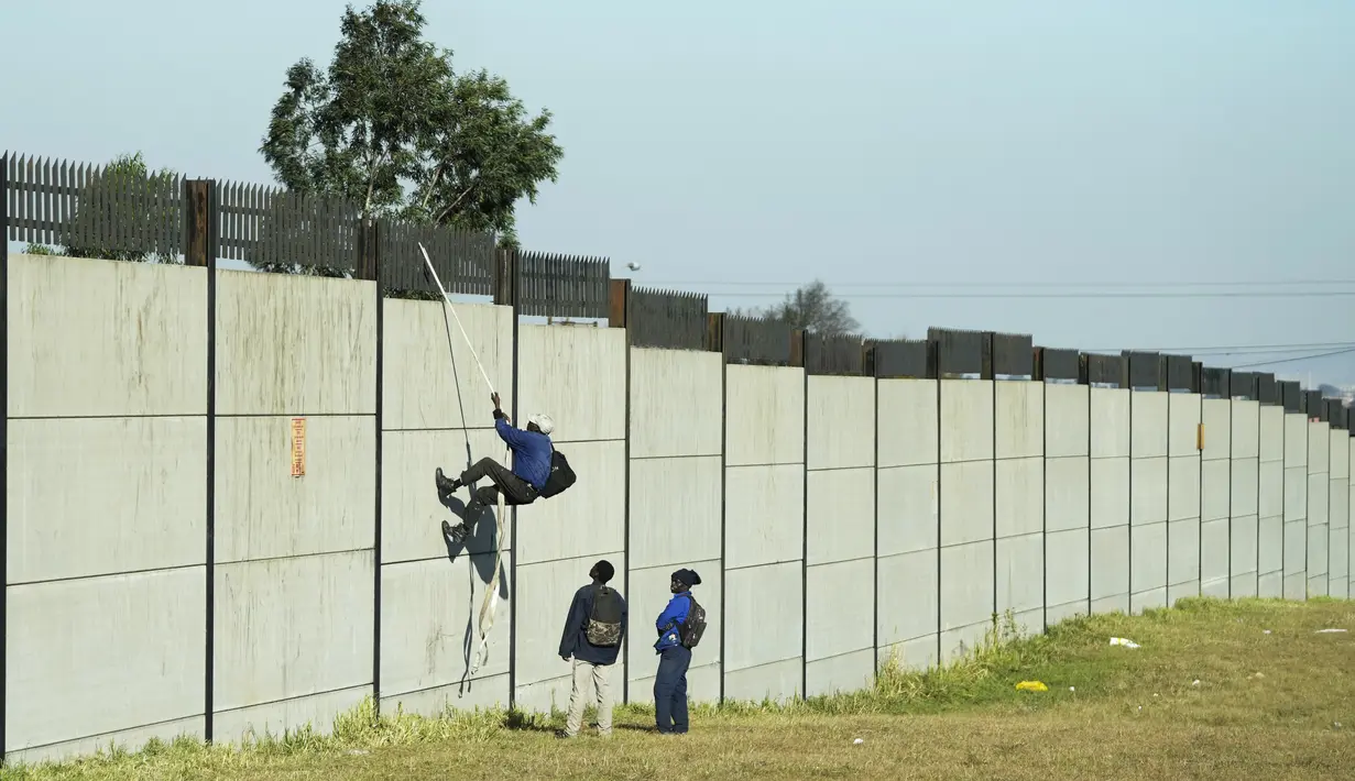 Seorang kolektor besi tua memanjat tembok untuk mencari besi tua untuk didaur ulang di pabrik pengolahan logam di Germiston, timur Johannesburg, Afrika Selatan (30/5/2022). Pengumpul besi tua di area tersebut melompat ke dinding beton untuk mengumpulkan besi tua dan kemudian menjualnya ke toko bekas. (AP Photo/Themba Hadebe)
