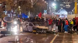 Suporter Maroko bersorak saat berdiri di samping mobil yang terbakar di Brussel, Belgia, 27 November 2022. Polisi harus menutup sebagian pusat Kota Brussel dan bergerak dengan meriam air serta gas air mata untuk membubarkan massa menyusul kerusuhan selama dan setelah Maroko menang 2-0 atas Belgia di Piala Dunia 2022. (AP Photo/Geert Vanden Wijngaert)
