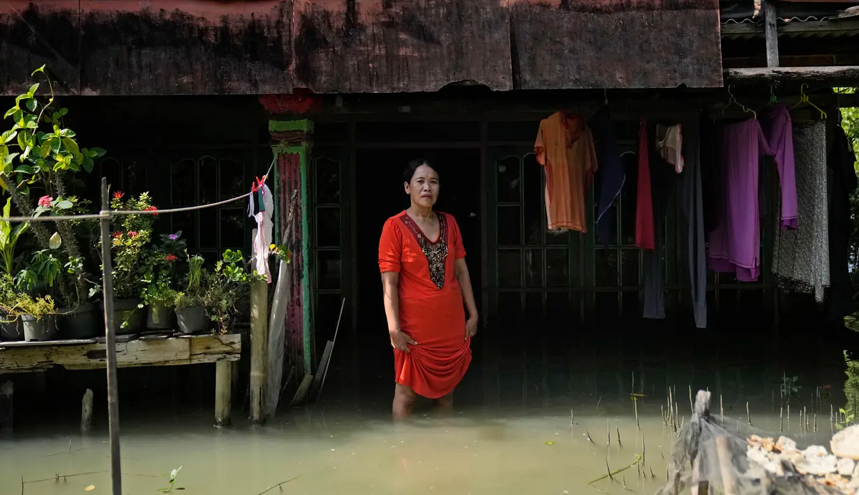 Zuriah berdiri di luar rumahnya yang terendam banjir di Mondoliko, Jawa Tengah, Indonesia, 1 Agustus 2022. Karena tidak mampu untuk pindah ke rumah baru, Zuriah tetap tinggal di rumah itu meski hampir semua tetangganya pindah. (AP Photo/Dita Alangkara)