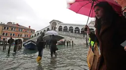 Warga berjalan dekat Jembatan Rialto saat gelombang pasang menerjang  di Venesia, Italia, Selasa (12/11/2019). Venesia dilanda banjir akibat gelombang pasang setinggi 127 cm. (AP Photo/Luca Bruno)