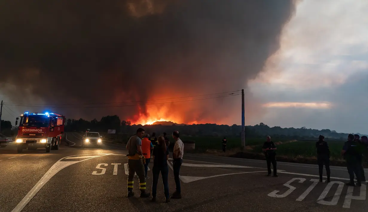 Petugas pemadam kebakaran, polisi, dan warga menyaksikan kebakaran hutan yang berkobar di Pumarejo de Tera dekat Zamora, Spanyol, 18 Juni 2022. Kebakaran hutan terbesar masih di luar kendali sore ini di Sierra de la Culebra, sebuah pegunungan di wilayah Castile dan Leon (barat laut), dekat perbatasan dengan Portugal. (CESAR MANSO/AFP)