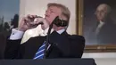 Presiden AS, Donald Trump meminum botol air mineral disela menyampaikan pidato di Ruang Diplomatik Gedung Putih, Rabu (15/11). Sementara itu warganet justru mengkritik Trump yang meminum air mineral impor merek Fiji Water. (MARK WILSON/GETTY IMAGES/AFP)