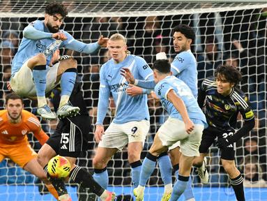 Pemain Manchester City, Josko Gvardiol, melakukan aksi loncat saat Phil Foden melepaskan tendangan ke gawang Leeds United pada pekan ke-13 Premier League 2025/2026 di Etihad Stadium, Sabtu (29/11/2025) malam WIB. (AFP/Oli Scarff)