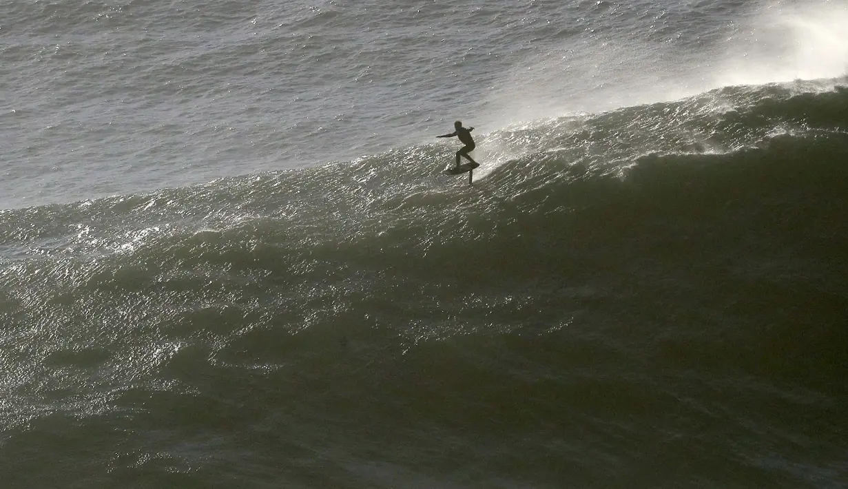 Seorang peselancar mengendarai papan hidrofoil menuruni gelombang selama sesi selancar derek di Praia do Norte atau Pantai Utara di Nazare, Portugal, Kamis (29/10/2020). (AP Photo/Pedro Rocha)