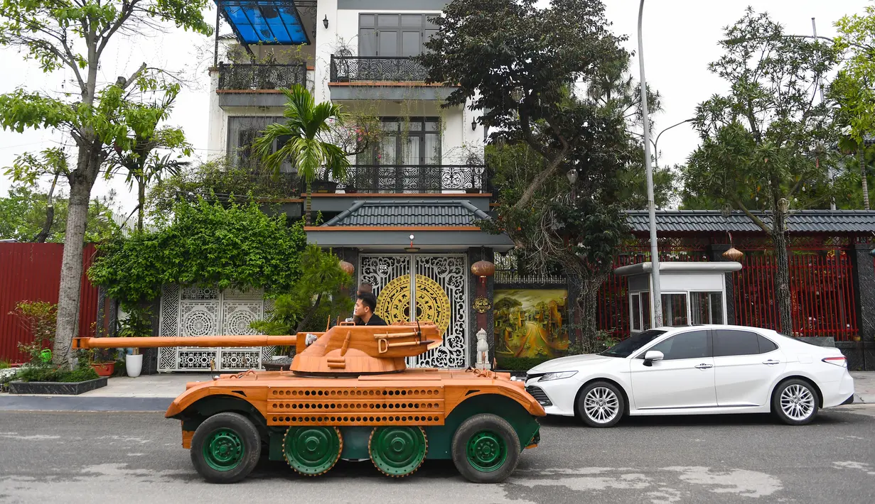 Truong Van Dao melewati sebuah rumah dengan tank kayu di daerah perumahan di provinsi Bac Ninh pada 28 Maret 2022. Seorang ayah di Vietnam telah menghabiskan ratusan jam dan menginvestasikan uangnya untuk mengubah mobil van tua menjadi tank kayu untuk putranya. (Nhac NGUYEN /AFP)