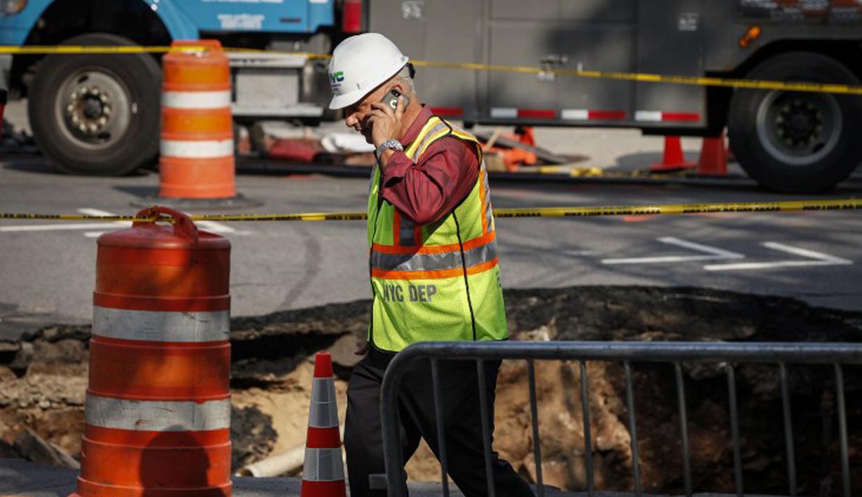 Seorang petugas berjalan di dekat lubang besar (sinkhole) di wilayah Brooklyn, New York, Selasa (4/8/2015). Lubang yang terbentuk di persimpangan pemukiman Sunset Park itu disebabkan erosi dan merusak pipa air serta aspal jalan. (AFP/Kena Betancur)