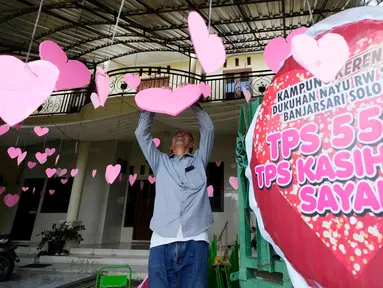 Seorang pria menghias simbol hati untuk Hari Valentine atau Hari Kasih Sayang di sebuah Tempat Pemungutan Suara (TPS) di Solo, Jawa Tengah, Selasa, 13 Februari 2024. (AP Photo/Achmad Ibrahim)