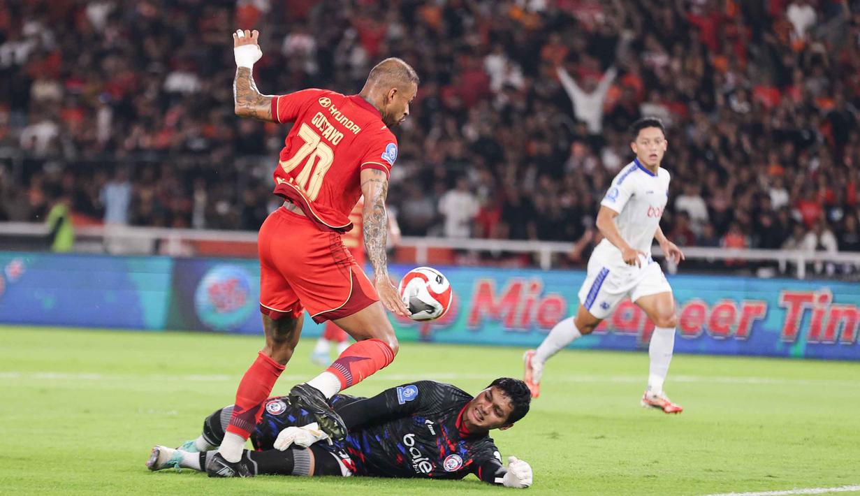 Persija tertinggal dari Persib Bandung di puncak dengan selisih enam angka. Tampak dalam foto, penjaga gawang Arema FC, Muhammad Adi Satryo (bawah) menahan pergerakan penyerang tengah Persija, Gustavo Almeida Dos Santos saat pertandingan pekan ke-20 BRI Super League 2025/2026 di Stadion Utama Gelora Bung Karno, Jakarta, Minggu (8/2/2026). (Bola.com/Abdul Aziz)