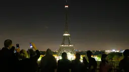 Pengunjung mengambil gambar saat pemadaman lampu Menara Eiffel di Paris, Rabu (24/5) dini hari. Hal tersebut dilakukan sebagai bentuk penghormatan dan duka cita atas serangan bom pada konser Ariana Grande di Manchester, Inggris. (AP Photo/Francois Mori)