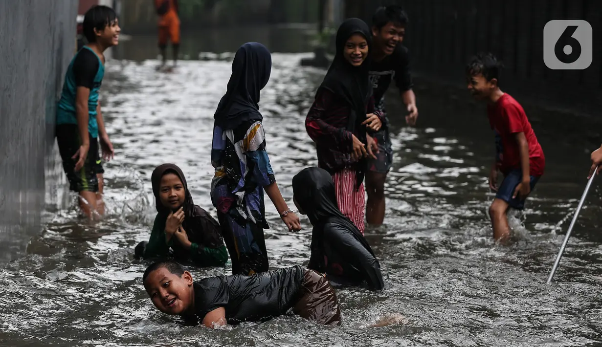 Anak-anak bermain air saat banjir merendam lingkungan rumah tempat tinggal mereka di kawasan kecamatan Kebayoran Baru, Jakarta, Senin (25/01/2021). Hujan deras yang mengguyur Jakarta hari ini, Senin (25/1) menyebabkan terjadinya banjir di kawasan permukiman tersebut. (Liputan6.com/Johan Tallo)