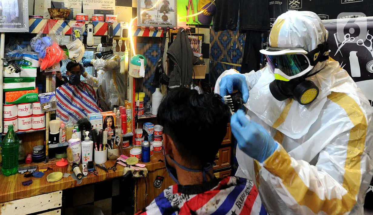 Seorang tukang cukur mengenakan alat pelindung diri (APD) saat memangkas rambut pelanggannya di Chemot Barbershop, Ciawi, Bogor, Jawa Barat, Minggu (5/4/2020). Penggunaan APD buatan sendiri tersebut merupakan sosialisasi kepada pelanggan. (merdeka.com/Arie Basuki)