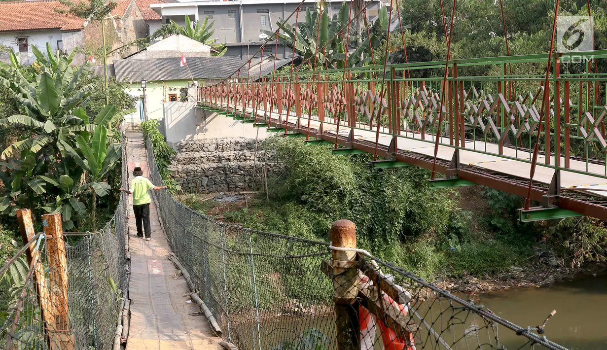 Warga berjalan di samping jembatan gantung yang diberi julukan Indiana Jones di Srengseng Sawah, Jagakarsa, Jakarta, Jumat (3/8). Pemprov DKI membangun jembatan Indiana Jones karena yang lama sudah tidak layak. (Liputan6.com/Immanuel Antonius)