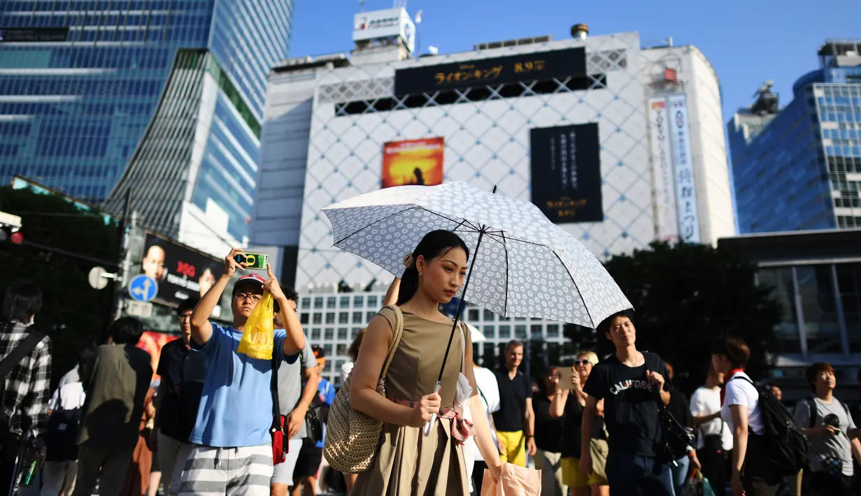 Seorang wanita menggunakan payung untuk melindungi dirinya dari sinar matahari selama gelombang panas saat melintas di distrik Shibuya Tokyo, Minggu (4/8/2019). Setelah menyerang beberapa wilayah di Eropa, suhu tinggi juga terjadi di Jepang. (Charly TRIBALLEAU / AFP)