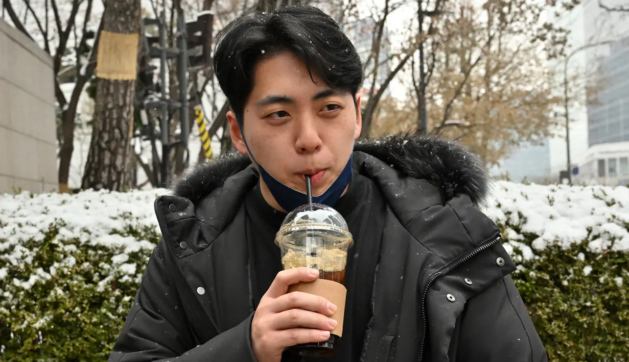 Gambar yang diambil pada 26 Januari 2023 ini menunjukkan akuntan Lee Dae-hee meminum es Americano selama wawancara dengan AFP di sebuah jalan di Seoul, Korea Selatan. Rata-rata orang Korea Selatan minum 353 cangkir per tahun, lebih dari dua kali lipat rata-rata global, menurut sebuah studi tahun 2019 oleh Hyundai Research Institute. (Jung Yeon-je / AFP)